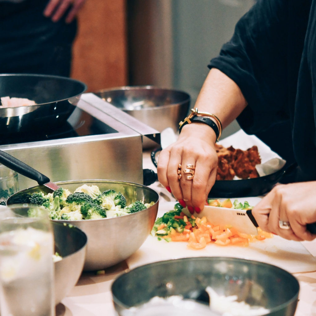 Eine Hand schneidet gerade Gemüse in einer Küche und ganz viele Schüssel sind schon mit unterschiedlichen geschnippelten Zutaten gefüllt