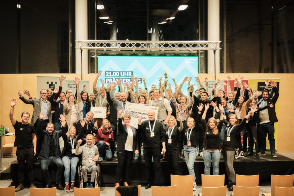 Auf dem Bild sind viele Personen vom Creators Camp for global ideas auf einer Bühne zu sehen. Die Leute halten alle ihre Hande in die Höhe.